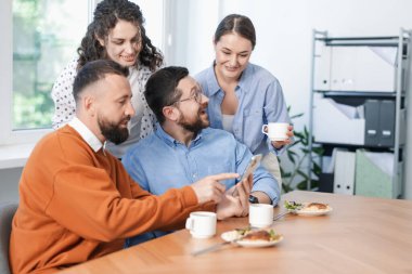 Ofiste öğle arasında iş arkadaşlarına akıllı telefondan bir şey gösteren bir adam.