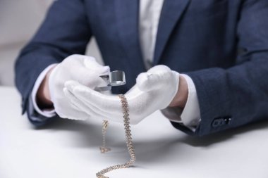 Beyaz masa içerisindeki lüks gerdanlığı değerlendiren eksper, yakın plan.