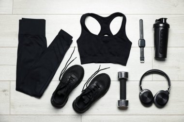 Spor kıyafetleri, spor ayakkabıları, kol saati, kulaklıklar ve dambıllar yere.