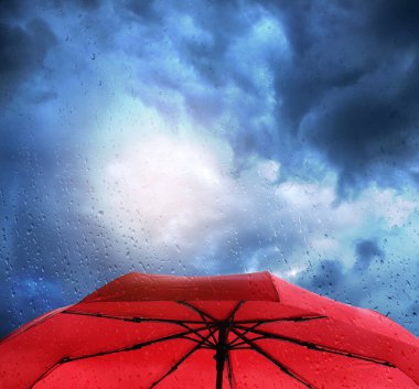 Bulutlu gökyüzünün altında kırmızı şemsiye, ıslak pencereden görüş. Fırtınalı hava
