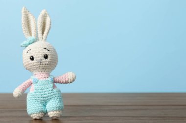 Ahşap masada açık mavi arka planda sevimli örülmüş oyuncak tavşancık. Metin için boşluk