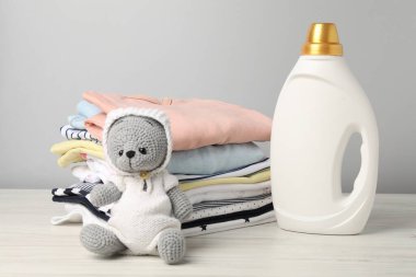 Bir şişe yumuşatıcı, bebek kıyafetleri ve beyaz arka planda açık ahşap masada oyuncak.