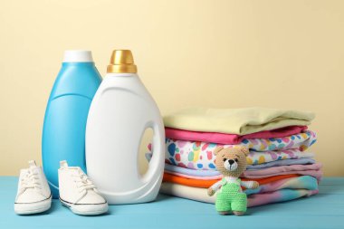 Kumaş yumuşatıcı şişeler, bebek kıyafetleri ve bej arka planda açık mavi ahşap masa üzerinde oyuncak
