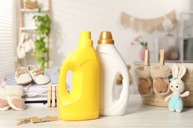 İçinde yumuşatıcılar olan şişeler, bebek kıyafetleri ve açık ahşap masa üzerindeki mandallar