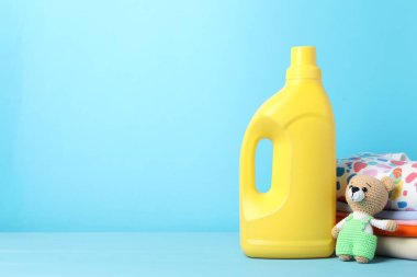 Şişe yumuşatıcı, bebek kıyafetleri ve açık mavi ahşap masada oyuncak. Metin için boşluk