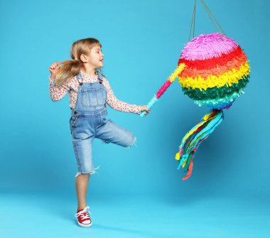 Mutlu kız parlak pinyatayı açık mavi arka planda kırıyor.