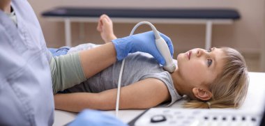 Sonograf, klinikte küçük kızın tiroid bezini ultrason muayenesi yapıyor.