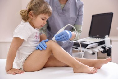Sonograf, klinikte küçük kızın dizinin ultrason muayenesini yapıyor.