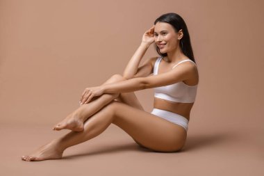 Beyaz iç çamaşırlı, pürüzsüz bir kadın. Bej arka planda epilasyon işleminden sonra.
