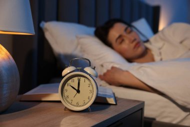 Evde uyuyan genç kadın, çalar saate ve kitaba odaklan.