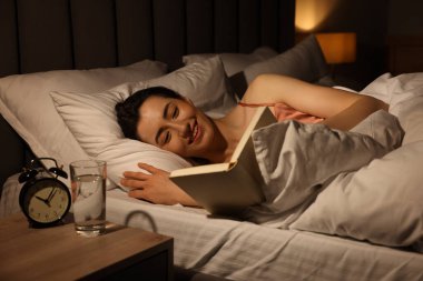 Evde yatakta kitap okuyan genç bir kadın.