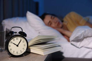 Evde uyuyan genç kadın, çalar saate ve kitaba odaklan.