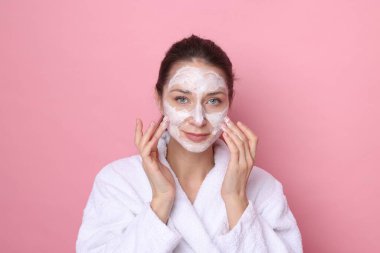 Spa günü. Güzel bir kadın pembe arka planda yüzüne maske takıyor.
