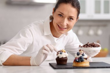Şekerci, masada bir parça çikolatayla kek süslüyor.