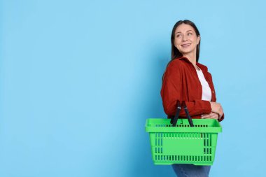 Açık mavi arka planda alışveriş sepeti olan gülümseyen kadın. Metin için boşluk