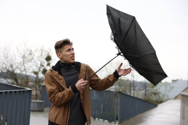 Kırık şemsiyeli bir adam açık havada yağmur altında rüzgarla savaşıyor.