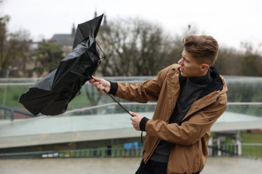 Kırık şemsiyeli bir adam açık havada yağmur altında rüzgarla savaşıyor.