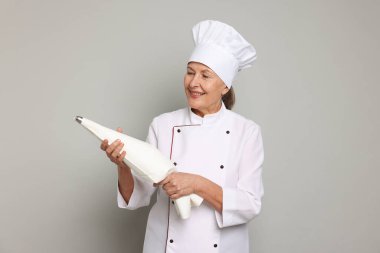 Açık gri arka planda krema torbası olan profesyonel pasta şefi.