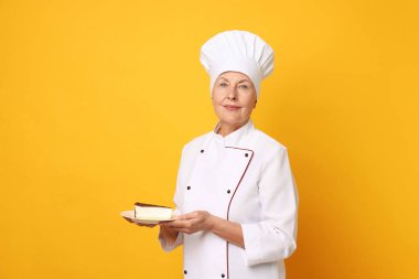 Turuncu arka planda kek dilimi olan profesyonel pasta şefi.