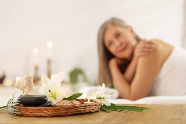 Üst düzey kadın masaj koltuğunda dinleniyor, farklı spa ürünlerine ve zambak çiçeklerine odaklanıyor.