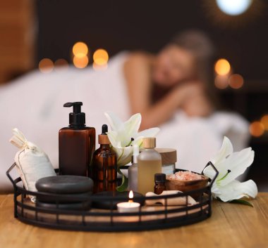 Üst düzey kadın masaj koltuğunda dinleniyor, farklı spa ürünlerine ve zambak çiçeklerine odaklanıyor.