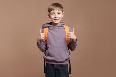 Sırt çantalı yakışıklı okul çocuğu kahverengi arka planda baş parmak gösteriyor.