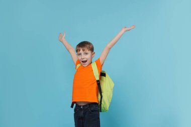 Açık mavi arka planda sırt çantası olan sevimli bir okul çocuğu.