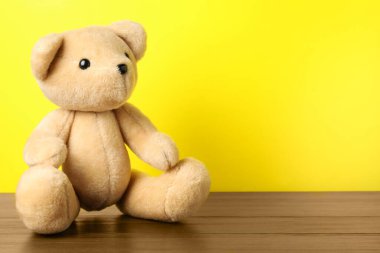 Sarı arka planda tahta masada sevimli bir oyuncak ayı. Metin için boşluk