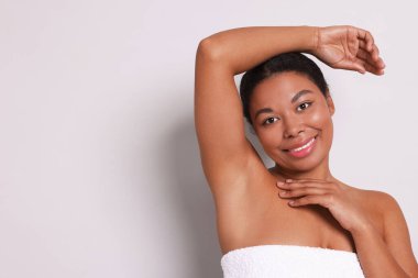 Açık gri arkaplanda epilasyon işleminden sonra kılsız koltuk altını gösteren kadın, metin için boşluk