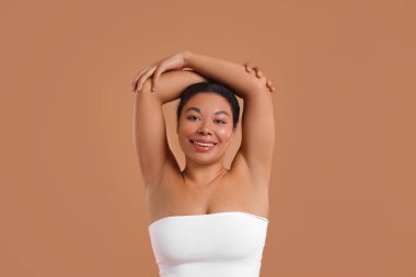 Bej arka planda epilasyon işleminden sonra kılsız koltuk altlarını gösteren kadın