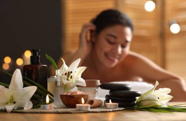 Güzel bir kadın masaj koltuğunda dinleniyor, farklı spa ürünlerine ve zambak çiçeklerine odaklanıyor.