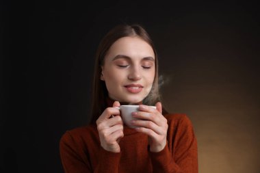 Kahverengi arka planda bir fincan kahveyle gülümseyen kadın.