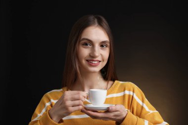 Kahverengi arka planda bir fincan kahveyle gülümseyen kadın.