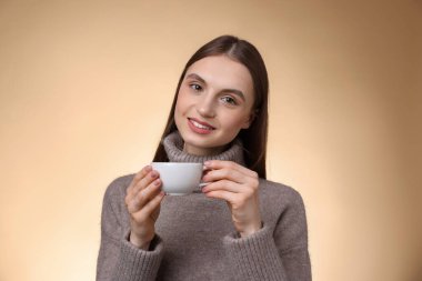 Bej renkli arka planda bir fincan kahveyle gülümseyen kadın