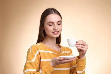 Bej renkli arka planda bir fincan kahveyle gülümseyen kadın