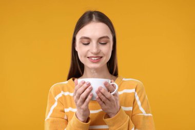 Sarı arka planda bir fincan kahveyle gülümseyen kadın.