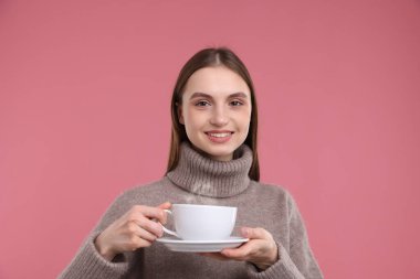 Pembe arka planda bir fincan kahveyle gülümseyen kadın.