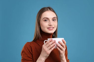 Açık mavi arka planda bir fincan kahveyle gülümseyen kadın.