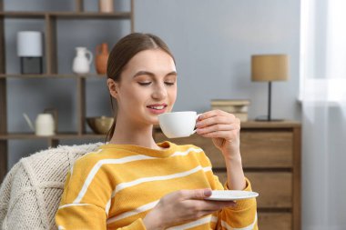 Evde bir fincan kahveyle gülümseyen kadın.