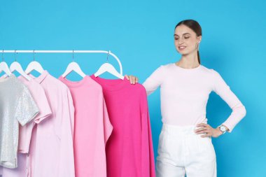 Gülümseyen moda tasarımcısı ve açık mavi arka planda giysileri olan askılar.