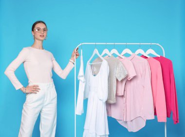 Moda tasarımcısı ve açık mavi arka planda giysileri olan askılar.