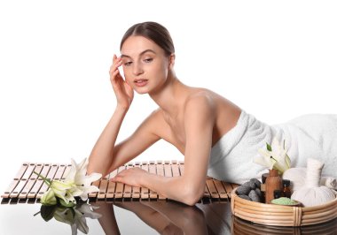 Beyaz arka planda bambu hasırında poz veren güzel bir kadın. Ayna yüzeyinde kaplıca ürünleri ve çiçekler