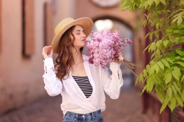 Güzel bir kadın, elinde bir buket leylak çiçekle şehir caddesindeki ağacın yanında.