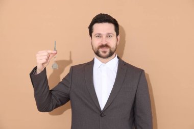 Emlakçının elinde bej arka planda ev şekilli anahtarlık var.