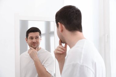 Yakışıklı adam aynada kendine bakıyor.