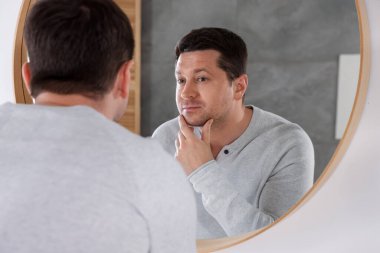 Yakışıklı adam aynada kendine bakıyor.