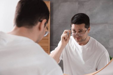 Yakışıklı adam aynada kendine bakıyor.