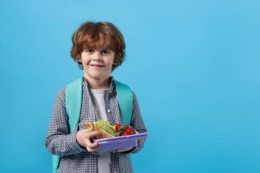 Açık mavi arka planda beslenme çantası olan şirin bir çocuk. Metin için boşluk