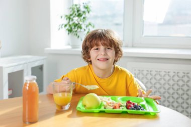 Okuldaki ahşap masada yemek yiyen şirin küçük çocuk.