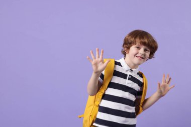 Menekşe arka planında sırt çantası olan sevimli bir okul çocuğu. Mesaj için yer var.